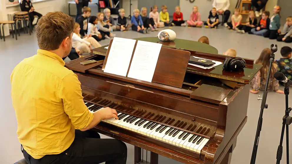 Børn øver til teaterkoncert sammen med en pianist bag et klaver