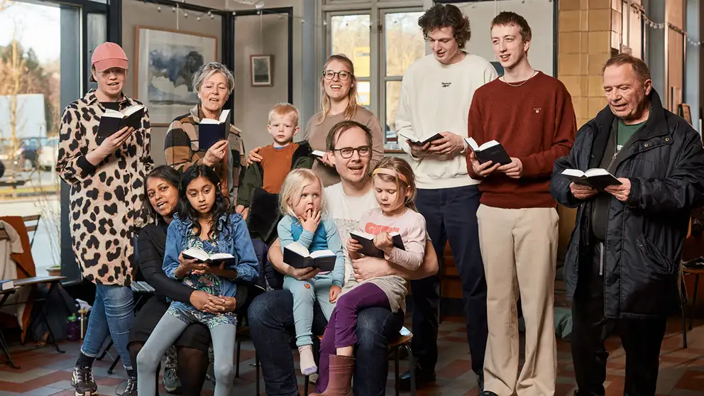 Billede af gruppe af voksne og børn, der synger sammen med sangbøger i hånden
