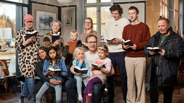 Billede af gruppe af voksne og børn, der synger sammen med sangbøger i hånden