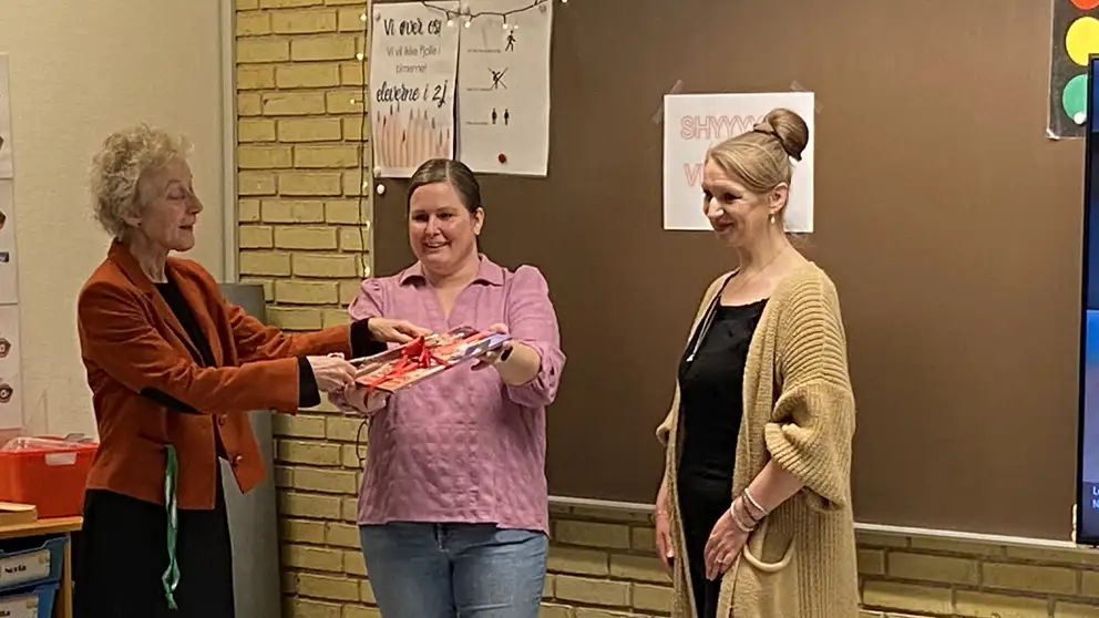 Billede af tre mennesker, der åbner en pakke med en bog i